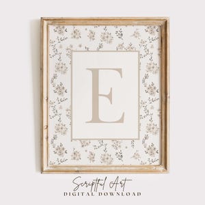 May include: A framed floral print featuring the letter "E" in a soft beige hue. The letter is centered on a cream-colored background, surrounded by a floral pattern in beige and green. The frame is a light, distressed wood. The text "Scriptful Art DIGITAL DOWNLOAD" is at the bottom.