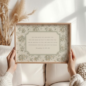 Könnte beinhalten: Ein gerahmter Druck mit einem floralen Muster in sanften Beige- und Grüntönen. Der Druck enthält ein zentrales Textfeld mit den Worten "THE LORD BLESS YOU AND KEEP YOU" und einen Bibelvers. Der Rahmen besteht aus hellem Holz.