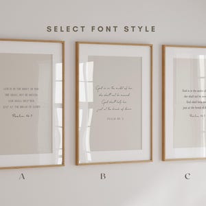 May include: Three vertical framed wall art prints with light wood frames, each displaying the text 'God is in the midst of her, she shall not be moved; God shall help her, just at the break of dawn. Psalm 46:5' in three different font styles labelled A, B, and C.