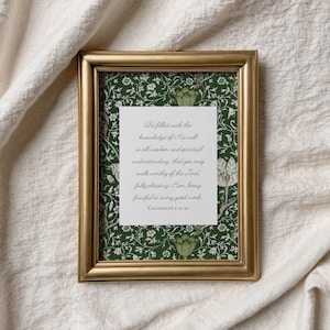 May include: A framed print with a gold-colored frame. The print features a white paper with handwritten text on a green floral patterned background. The text is a religious quote from Colossians 1:9-10.