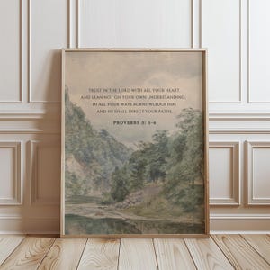Könnte beinhalten: Gerahmter Kunstdruck mit einer Landschaftsmalerei mit Fluss und Bäumen. Das Kunstwerk hat eine Vintage-Ästhetik und enthält den Text "TRUST IN THE LORD WITH ALL YOUR HEART... PROVERBS 3: 5-6" in einer Serifenschrift. Der Rahmen ist hellbraun.