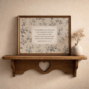 May include: A framed print with a floral pattern and the text "The steadfast love of the Lord never ceases; His mercies never come to an end; they are new every morning; great is Your faithfulness." displayed on a wooden shelf.