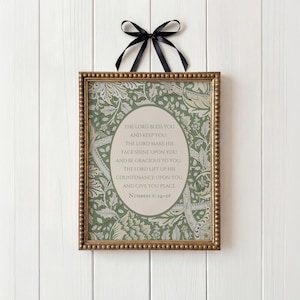 Pode incluir: Um pendente de parede retangular numa moldura dourada com contas e um padrão floral verde e creme. Um oval central contém o texto: THE LORD BLESS YOU AND KEEP YOU; THE LORD MAKE HIS FACE SHINE UPON YOU, AND BE GRACIOUS TO YOU; THE LORD LIFT UP HIS COUNTENANCE UPON YOU, AND GIVE YOU PEACE. NUMBERS 6: 24-26. Uma fita preta está presa no topo.