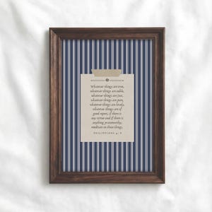May include: A framed print with a dark wood frame. The background features vertical navy blue and white stripes. A beige paper with text is taped to the center. The text reads "Whatever things are true...Philippians 4:8."