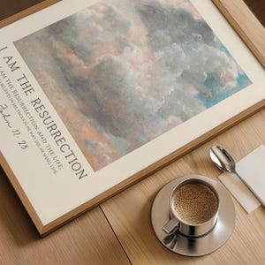 May include: A framed print with a watercolor painting of clouds in shades of blue, pink, and gray. The text "I AM THE RESURRECTION AND THE LIFE. HE THAT BELIEVES IN ME, THOUGH HE MAY DIE, HE SHALL LIVE. John 11:25" is printed below the painting.
