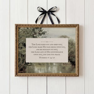 Könnte beinhalten: Ein rechteckiger Wandbehang mit einem goldfarbenen Perlenrahmen und einer schwarzen Schleife oben. In der Mitte befindet sich eine beige Karte mit dem Text: The Lord bless you and keep you; the Lord make His face shine upon you, and be gracious to you; the Lord lift up His countenance upon you, and give you peace. Numbers 6: 24-26.