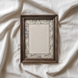 May include: A framed print of Psalm 91, featuring a decorative floral border in cream and gray. The text is in a classic serif font on a beige background, encased in a dark brown wooden frame. The print is displayed on a white fabric surface.