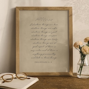 Può includere: Una stampa incorniciata con il testo "Whatever things are true..." in scrittura nera. La stampa è in una cornice di legno chiaro e poggia su una superficie di legno. Un paio di occhiali e un libro sono in primo piano.