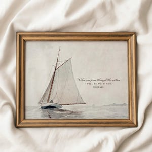 Op de afbeelding: Een ingelijste aquarelprint van een zeilboot op het water. De boot heeft een wit zeil en een bruine mast. Het frame is lichtbruin van kleur. De tekst op de print luidt: "Wanneer je door het water gaat, zal Ik bij je zijn. Jesaja 43:2."