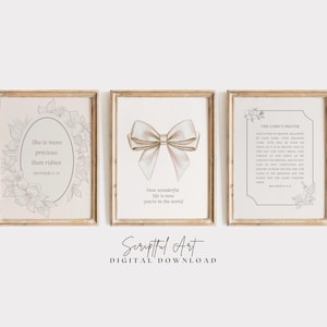 Op de afbeelding: Drie ingelijste kunstdrukken met inspirerende citaten en bloemaccenten. De prints tonen een strik, een bloemenontwerp met tekst en een ingelijste tekst van "The Lord's Prayer". De frames hebben een lichte houten afwerking.