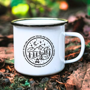 May include: White enamel camping mug with a black design featuring a mountain scene, a campfire, a tent, and the text "Commit to the Lord whatever you do, and your plans will succeed."  Proverbs 16:3