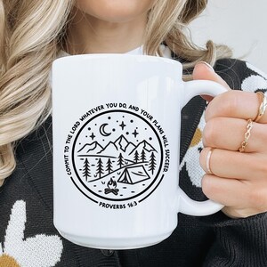 May include: White ceramic mug with a black and white design featuring a mountain scene with a campfire and a tent. The text "Commit to the Lord whatever you do, and your plans will succeed - Proverbs 16:3" is printed on the mug.