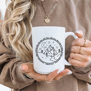 May include: White ceramic mug with a black and white illustration of a mountain range, moon, and stars. The text "GOD IS WITHIN HER SHE WILL NOT FALL GOD WILL HELP HER AT BREAK OF DAY" and "PSALMS 46:5" are printed on the mug.