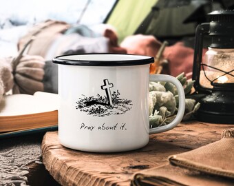Peut inclure: Une tasse en émail blanc avec un bord et une poignée noirs. La tasse est ornée d'une illustration en noir et blanc d'une croix dans une tombe avec le texte "Priez à ce sujet."