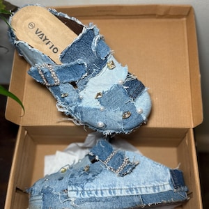 May include: Denim clogs with a patchwork design, embellished with pearls and rhinestones. The clogs have a buckle closure and are in a cardboard box. The brand name "VAYFIO" is visible on the insole.