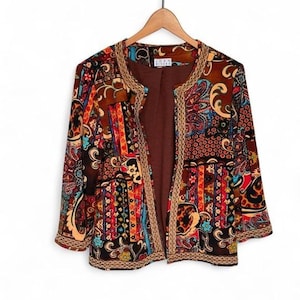 May include: A long-sleeve open-front jacket featuring a multi-colored patchwork pattern with paisley, floral, and geometric motifs in shades of brown, red, blue, and gold. The garment has a solid brown interior lining and gold-toned trim.