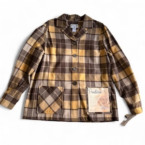 May include: A long-sleeve jacket in a brown and yellow plaid pattern with a notched collar and four dark buttons down the front. It features two large square patch pockets and a Pendleton 49er brand tag attached to the lower right pocket.