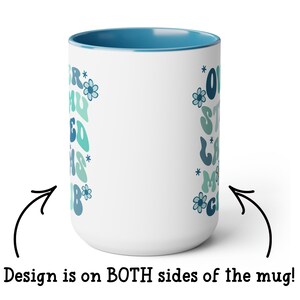 May include: White ceramic mug with a blue rim. The mug has a design on both sides featuring a blue and green retro-style font that says "Our Staycation Mood" with flowers and stars. The design is on both sides of the mug.
