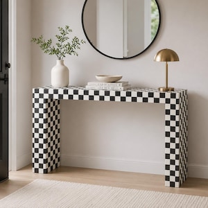 May include: A rectangular console table featuring a bold black and white checkered pattern across its entire surface. The table has a clean, boxy silhouette with two wide, matching checkered legs that provide a sturdy base for the tabletop.