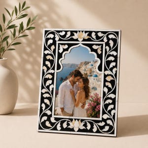 Könnte beinhalten: Rechteckiger Fotorahmen mit einem schwarz-weißen Blumendesign. Der Rahmen hat eine zentrale Bogenform, die ein sich umarmendes Paar zeigt. Der Rahmen ist aus Holz gefertigt und hat eine dekorative Einlage.