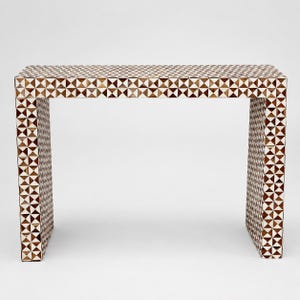Puede incluir: Una consola rectangular con un patrón geométrico. La superficie y las patas de la mesa están cubiertas con un mosaico de triángulos y cuadrados marrones, blancos y beige. La mesa es un mueble decorativo.