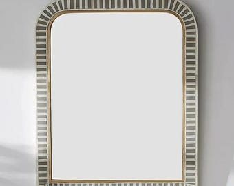 May include: Rectangular wall mirror with a rounded top. The frame has a repeating pattern of grey and white vertical stripes. The mirror's interior has a gold-coloured border.
