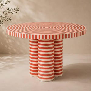 May include: A round table featuring a vibrant red and white striped pattern across the circular top and the three cylindrical legs. The tabletop displays a concentric circular design, while the legs are decorated with horizontal stripes.