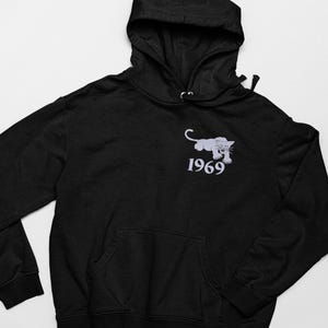 Könnte beinhalten: Schwarzer Kapuzenpullover mit Kängurutasche. Mit einem hellgrauen Panther-Motiv und der darunter aufgedruckten Zahl "1969". Der Hoodie hat einen Kordelzug sowie gerippte Bündchen und Saum.