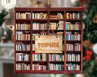 May include: A wooden ornament shaped like a bookshelf filled with colorful books. A wooden sign with the name "SOPHIA" hangs in front. The ornament has a gold string for hanging and the words "CUSTOMIZE DESIGN" at the bottom.