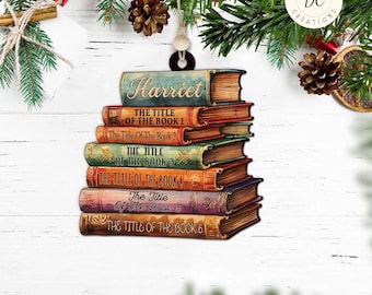 May include: A personalized Christmas ornament featuring a stack of six books with the name "Harriet" on the top book. The books have various titles, including "The Title of the Book 1", "The Title of the Book 2", and so on. The ornament is made of wood and has a rustic, vintage look.