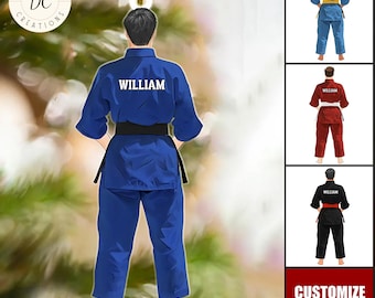 May include: A blue karate uniform ornament with the name "WILLIAM" printed on the back. The ornament features a black belt and is hanging from a gold string. Additional color variations of the uniform are shown in the image.