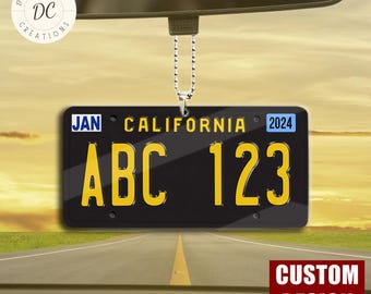 Puede incluir: Accesorio para coche con placa de matrícula de California negra con letras y números amarillos, incluyendo "ABC 123" y "CALIFORNIA". La placa también muestra "JAN" y "2024". El accesorio cuelga de una cadena.