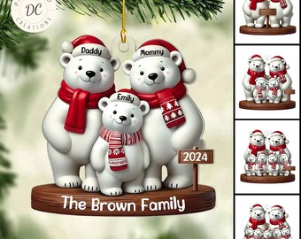 Puede incluir: Adorno familiar de osos polares con bufandas rojas y gorros de Papá Noel. Los osos están sobre una base de madera con el texto "The Brown Family" y "2024". El adorno es personalizable.