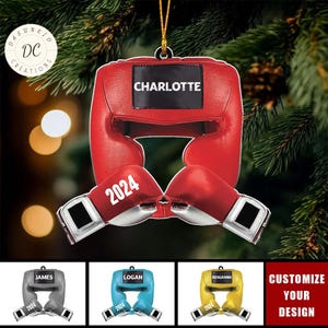 May include: A red boxing helmet and gloves ornament with the name "CHARLOTTE" and the year "2024" printed on it. The ornament is hanging in front of a Christmas tree. Additional color options are shown below.