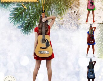 Może przedstawiać: Ozdoba choinkowa z personalizacją przedstawiająca kobietę trzymającą gitarę akustyczną. Gitara jest ozdobiona imieniem "SHOPIA", a ozdoba może być spersonalizowana imieniem, numerem i kolorem.