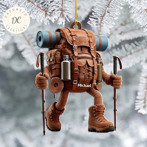 Könnte beinhalten: Brauner Wanderer-Ornament mit Rucksack, Wanderschuhen und Trekkingstöcken. Der Rucksack hat eine blaue Isomatte befestigt. Das Ornament trägt den Namen "Michael". Das Ornament hängt an einer goldenen Schnur.