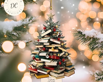 May include: Christmas tree ornament shaped like a tree made of books, decorated with red and gold ornaments. A gold star tops the tree. The ornament has a small sign that reads "Sam 2025". The ornament hangs from a gold string.