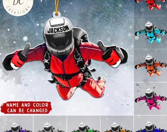 Può includere: Un ornamento natalizio personalizzato con un paracadutista in tuta e casco rossi con il nome "Jackson". L'ornamento ha un cordino dorato per appenderlo e il testo "NAME AND COLOR CAN BE CHANGED". Sono mostrati paracadutisti aggiuntivi in vari colori.