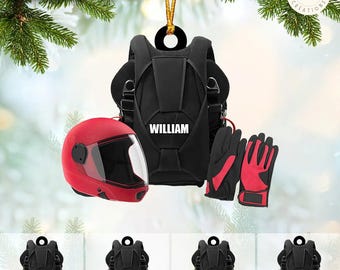 Può includere: Addobbo natalizio personalizzato con uno zaino nero con il nome "William", un casco rosso e guanti rossi. L'addobbo è appeso a un ramo d'albero.