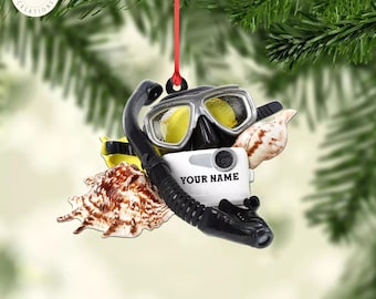 May include: A white and black scuba diving ornament with a seashell, a diving mask, and a snorkel. The ornament has a white tag that says "YOUR NAME".