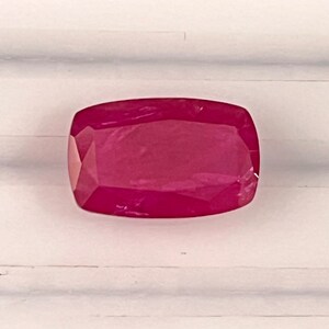 May include: A deep pink, faceted gemstone with a rectangular shape.