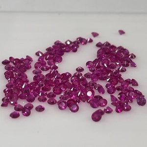 May include: A large group of loose, round, pink gemstones. The gemstones are scattered on a white surface.