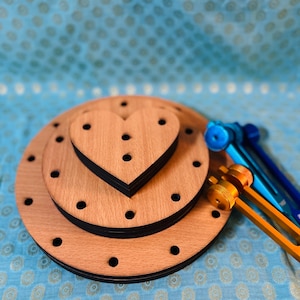May include: A wooden cake stand with three tiers, including a heart-shaped top tier. The stand has a natural wood finish with black accents. Several tuning forks in blue and orange are placed to the side.