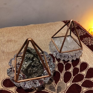 May include: Two clear glass geometric pyramids with gold metal frames. The pyramids are filled with crystals. One pyramid contains clear crystals and the other contains dark gray crystals.