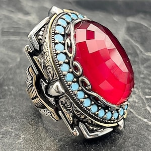Peut inclure: Une bague en argent avec une grande pierre rouge sertie d'une bordure de pierres turquoise. La bague est ornée de détails complexes et d'un accent doré.