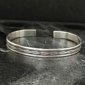 May include: A silver bangle bracelet with a braided design.