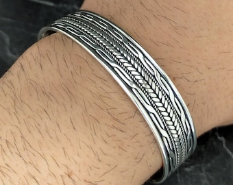 May include: A silver bracelet with a braided design. The bracelet is open and has a simple, elegant look.