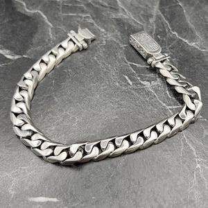 May include: A silver chain bracelet with a detailed clasp. The chain is made of interlocking links.