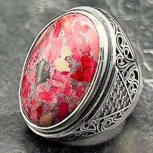 Op de afbeelding: Een zilveren ring met een ovale roze en witte edelsteen, gezet in een gedetailleerde zilveren band.
