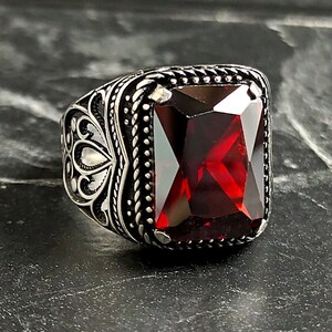 Puede incluir: Un anillo de plata con un diseño adornado y una gran piedra preciosa cuadrada roja.